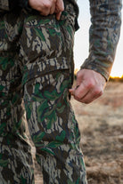 Hunter adjusting side vent zipper on North Mountain Gear Advantis lightweight Mossy Oak Greenleaf camo hunting pants during a hunt.